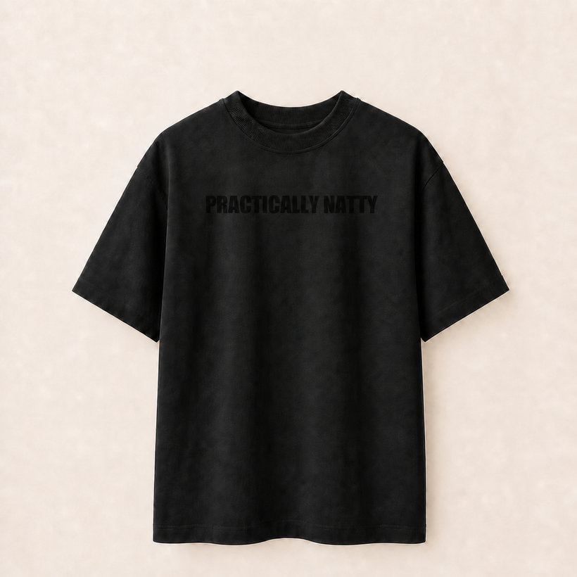 Black Practically Natty tee front with balanced readable tonal black block wordmark on a warm ivory studio background