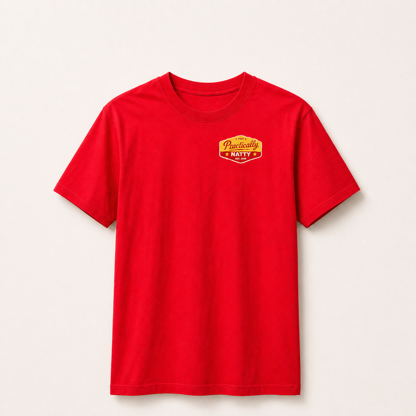 Red Practically Natty tee front with gold and red PNP badge on a warm ivory studio background